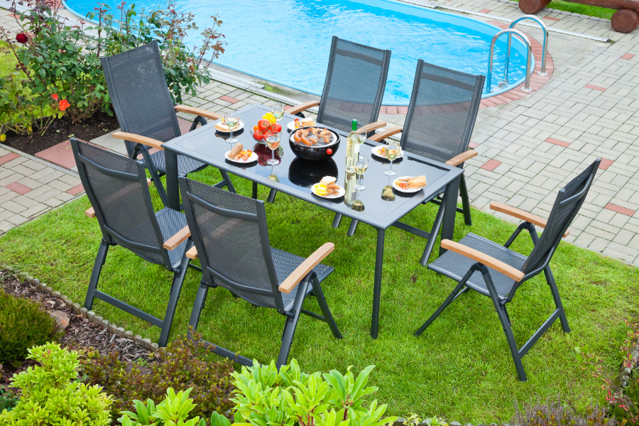 a set metal outdoor dining table and chairs next to a pool in a backyard